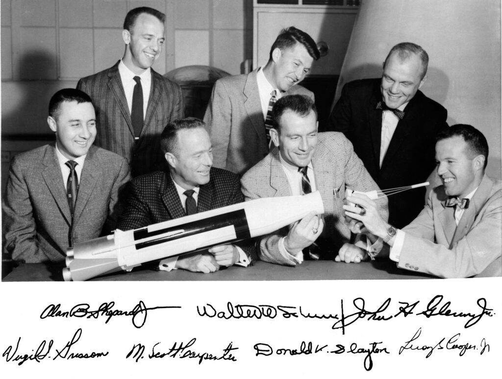 Foto der Mercury Seven mit dem Modell einer Rakete, unterschrieben von allen Mitgliedern
